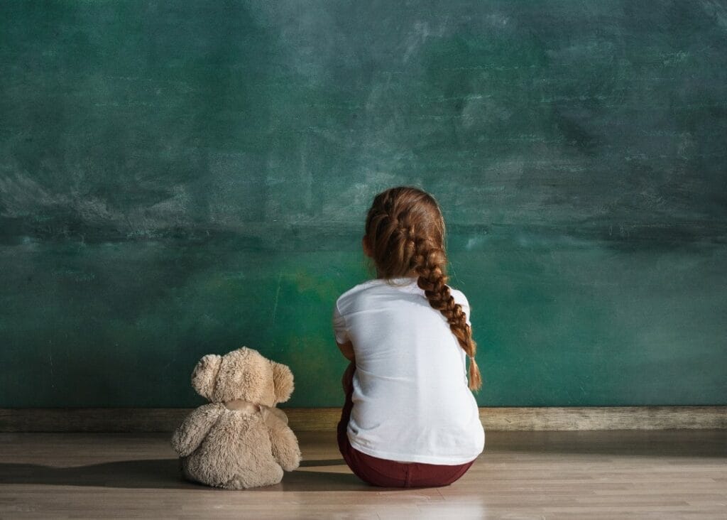 Girl next to teddy bear staring at wall