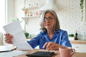 Elderly woman with document and calculator at kitchen table