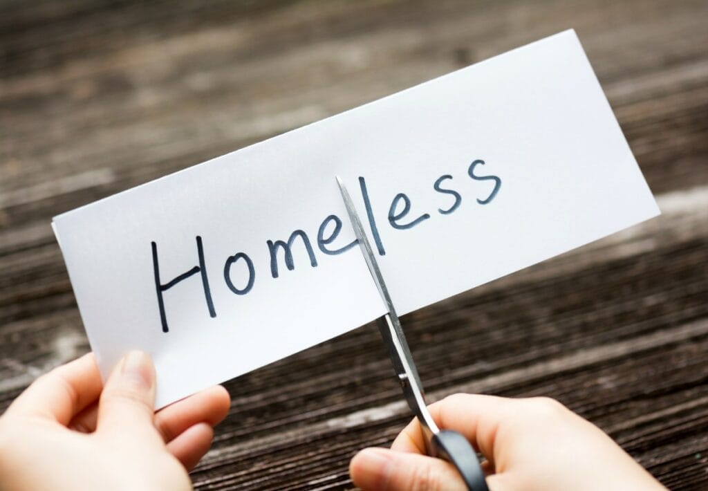 Person using scissors to cut a piece of paper with the word "Homeless" on it in half