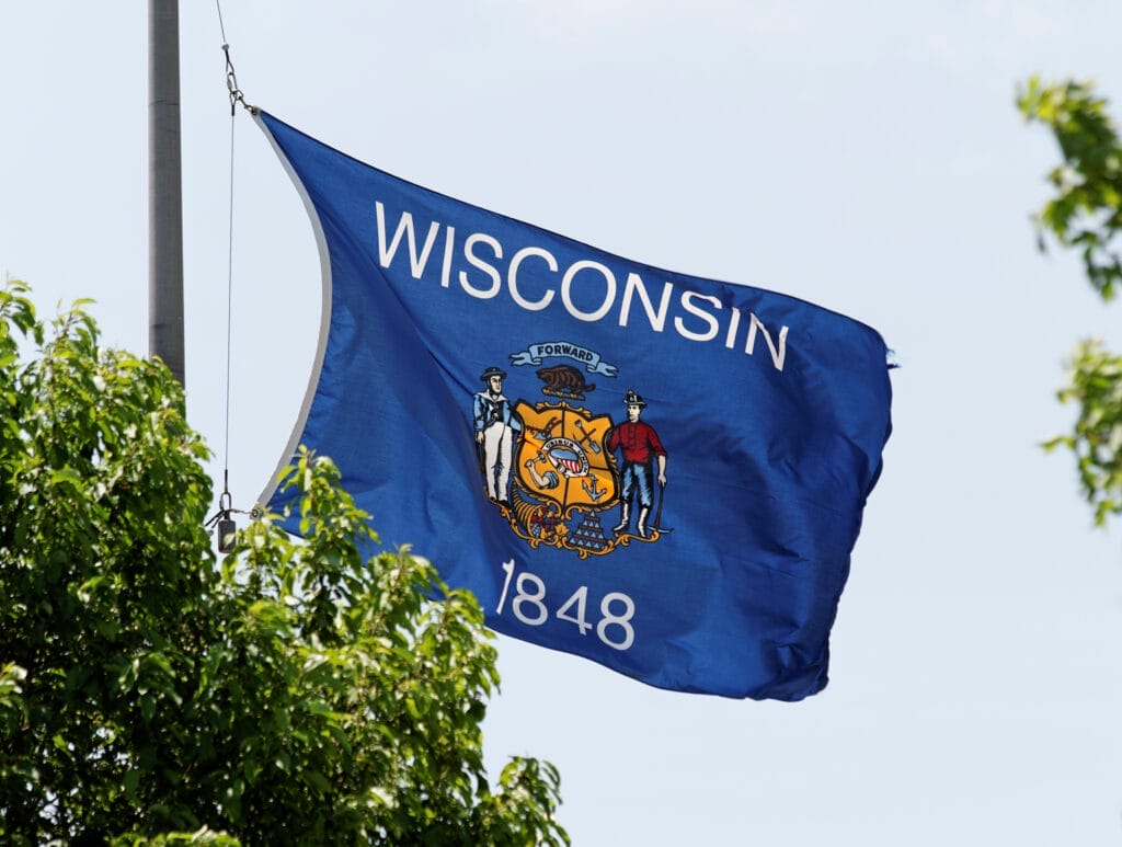 Wisconsin state flag flying over shrubbery