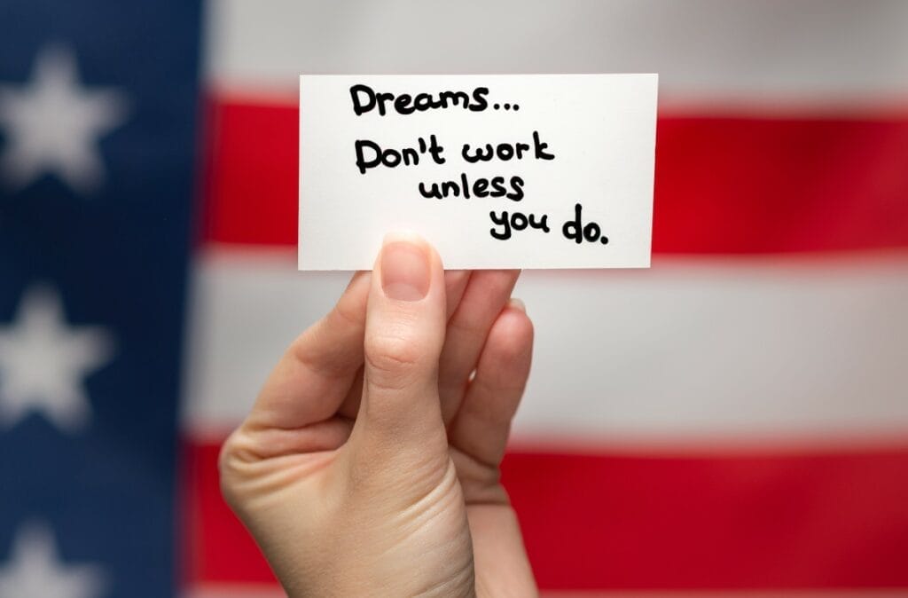 Hand holding sign about working hard for dreams set against a background of the American flag