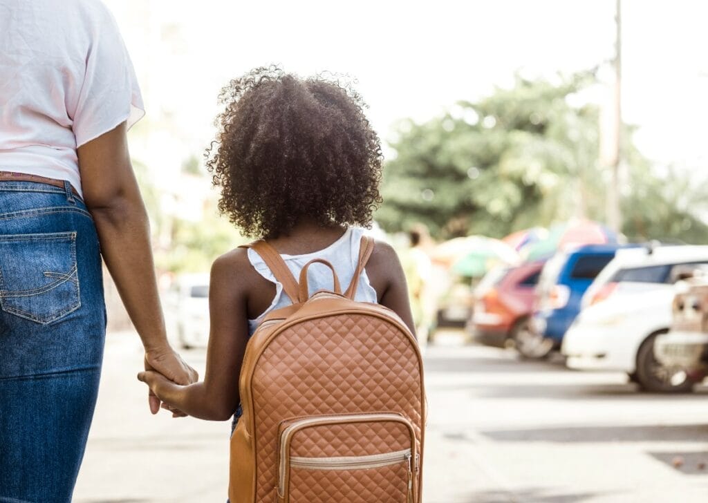 Young Black girl wearing backpack and holding hand of mother as the family’s education freedom may be affected by Wisconsin’s school choice lawsuit