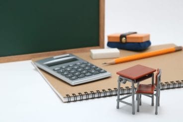 Figure of a student desk next to notebook, pencil, blackboard, and calculator