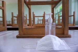 Classroom with no students, chairs flipped atop desks, a bottle of hand sanitizer, and a COVID facemask