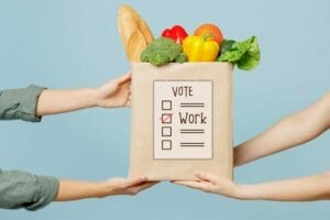 One set of hands handing bag of groceries to another set of hands with a graphic ballot on the grocery bag indicating Wisconsin’s referendum to requirement work for food stamps receipt.