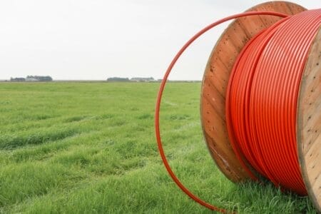 Large reel of broadband cable in a rural field with farmhouse in the background
