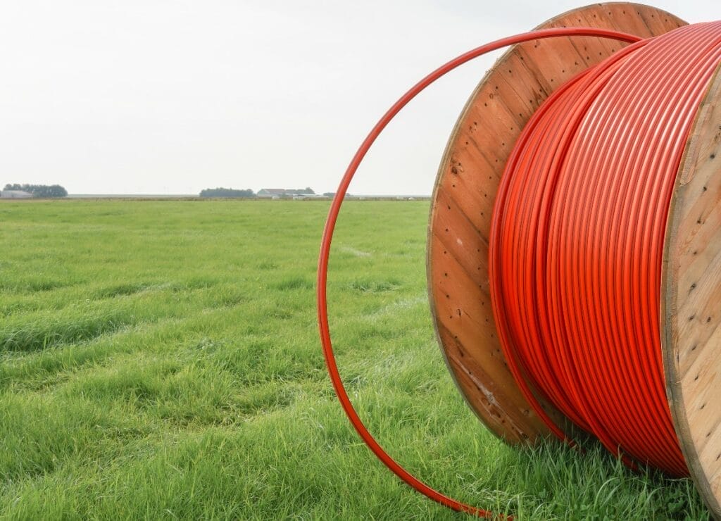 Large reel of broadband cable in a rural field with farmhouse in the background