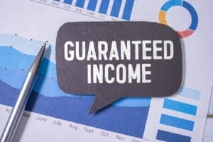 Paper with financial graphs and term "guaranteed income" overlayed on a thought ballon.