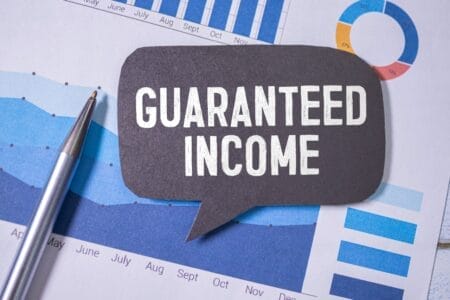 Paper with financial graphs and term "guaranteed income" overlayed on a thought ballon.