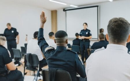Police officer in training raising hand to ask a question in classroom with other recruits.