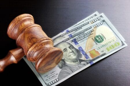 A judge’s gavel and three $100 bills across a dark background