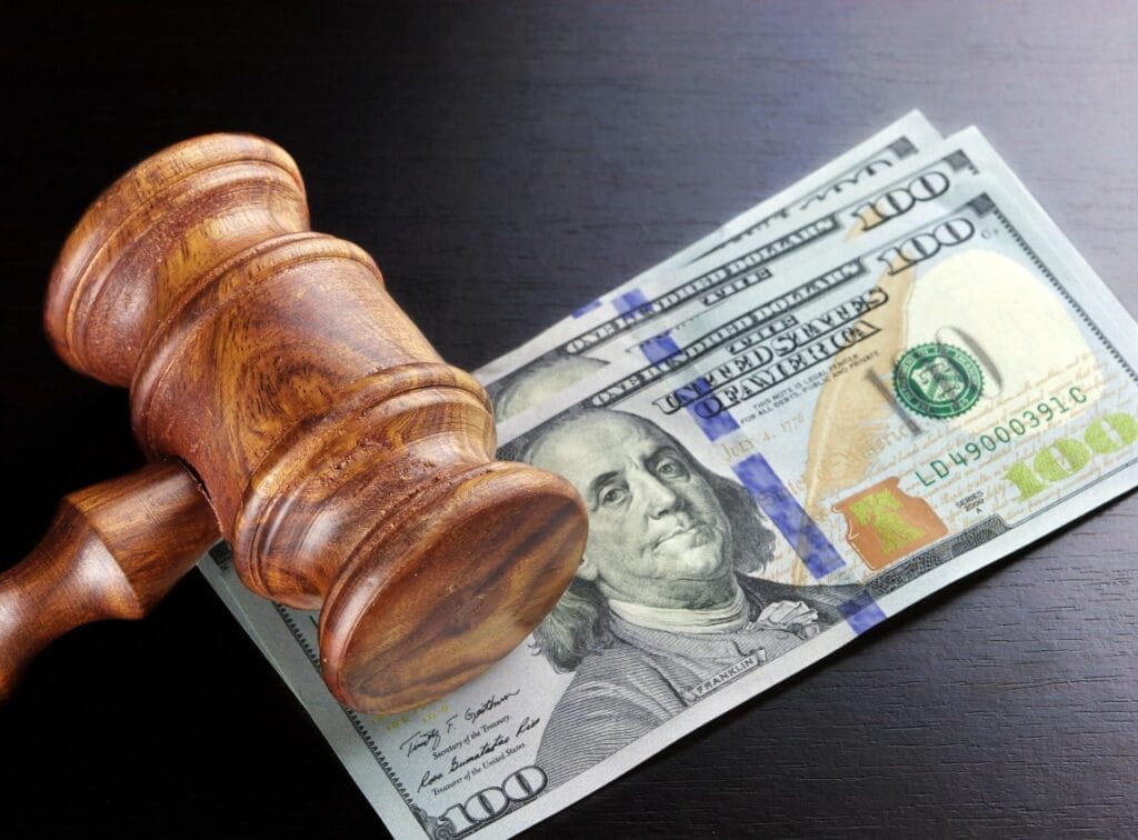 A judge’s gavel and three $100 bills across a dark background