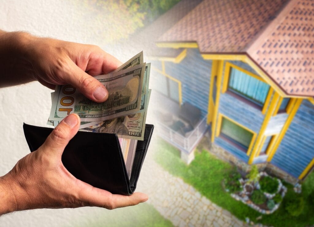 Person removing $100 bills from wallet against a background of a single-family home