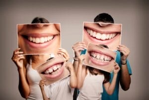 Image of family of four holding enlarged photos of their smiles in front of their faces.