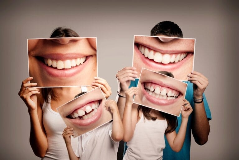Image of family of four holding enlarged photos of their smiles in front of their faces.