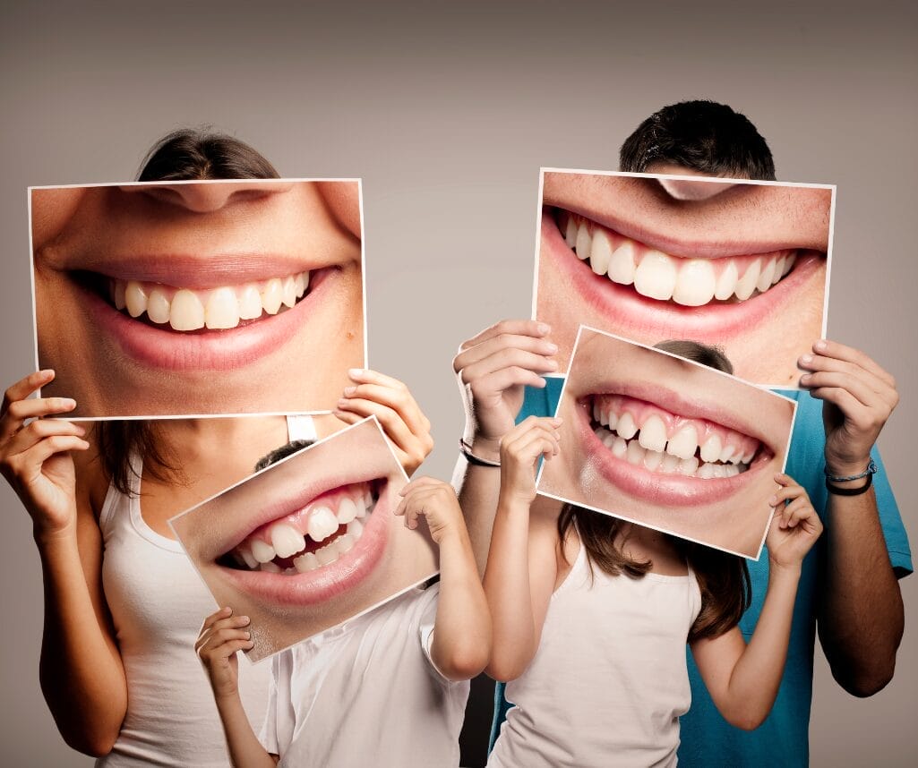 Image of family of four holding enlarged photos of their smiles in front of their faces.