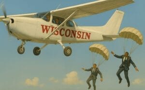Generate image of an airplane with the word "Wisconsin" painted aside and two business-attired accountants parachuting to escape.